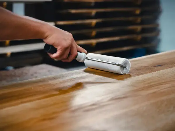 Main d'artisan appliquant une couche de vernis sur une table en bois avec un rouleau, pour la protéger et la sublimer.